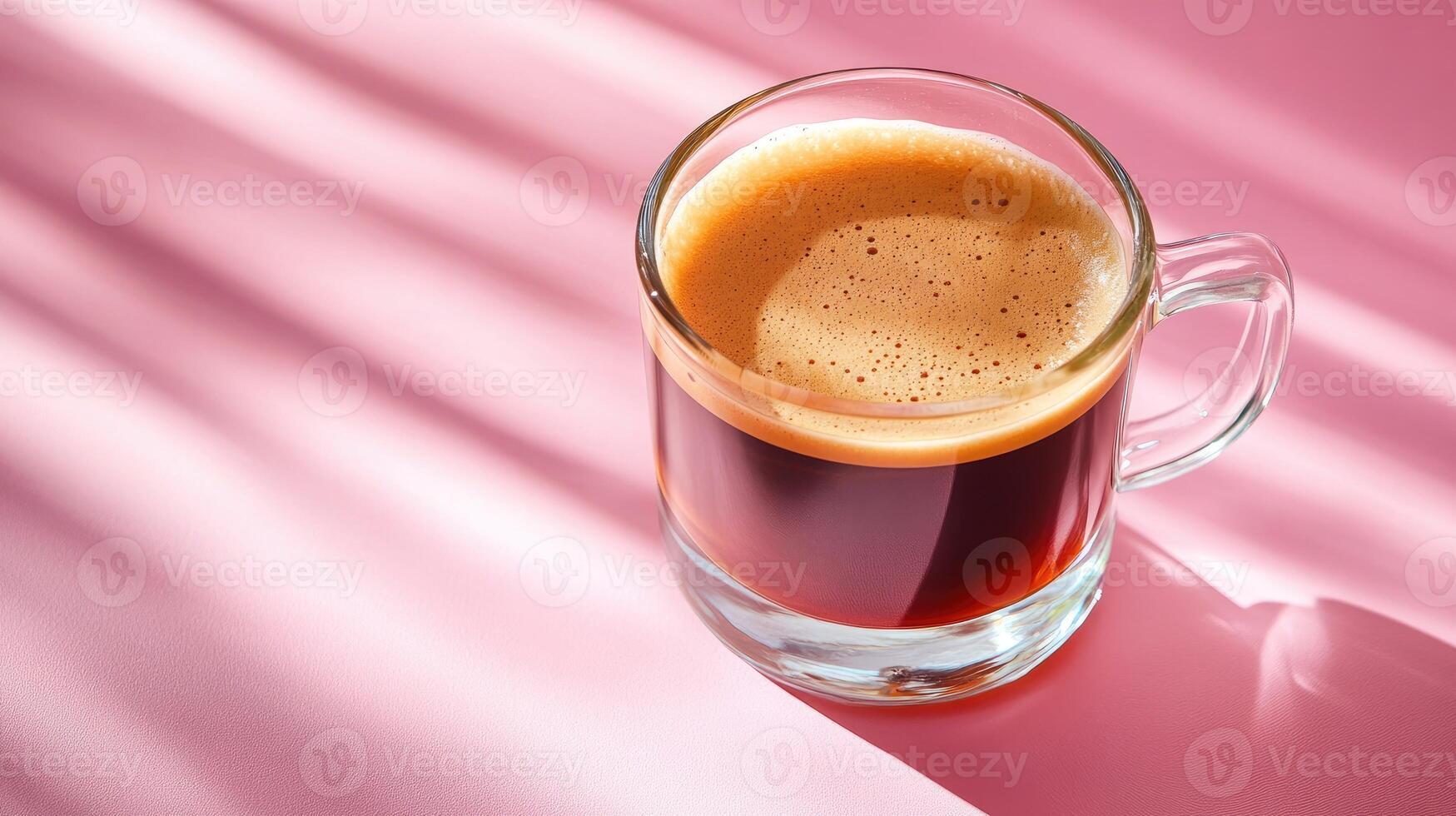 Glass cup of hot espresso coffee sitting on pink background with window light creating shadows photo