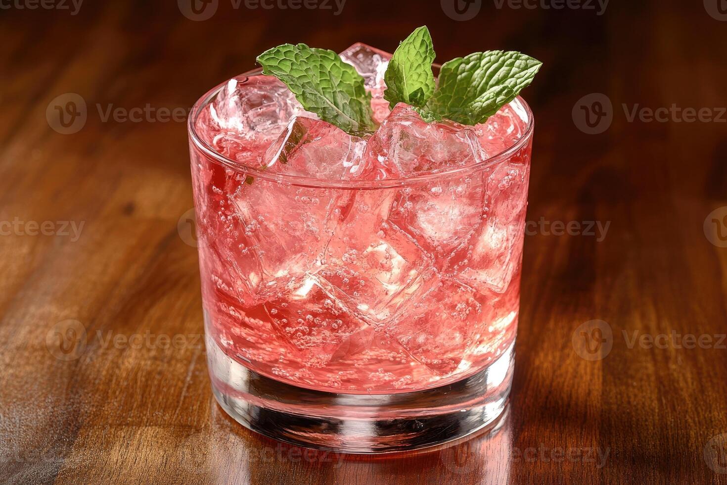 Refreshing pink cocktail garnished with ice and mint on wooden table photo