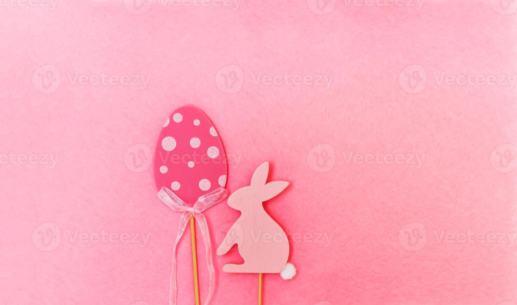 Easter composition with traditional decor. Wooden decorative egg and rabbit figures on soft light pink background. photo
