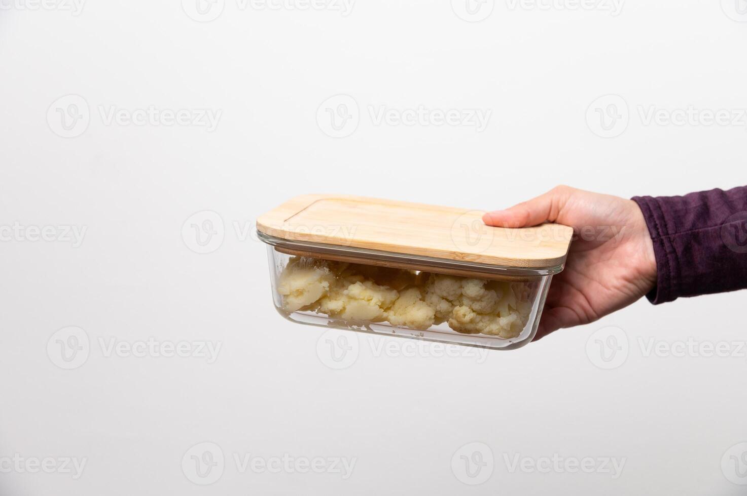 Using reusable tableware for food. Female hand holding glass container with wooden lid with her lunch against gray wall photo