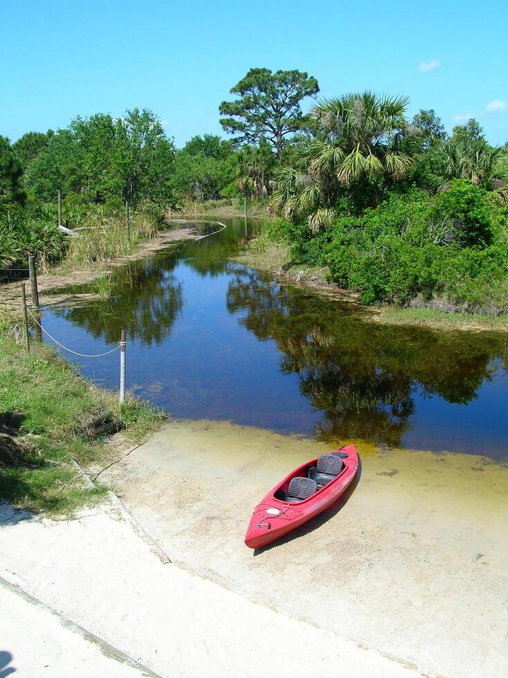 A red kayak sits on the sand next to a river photo