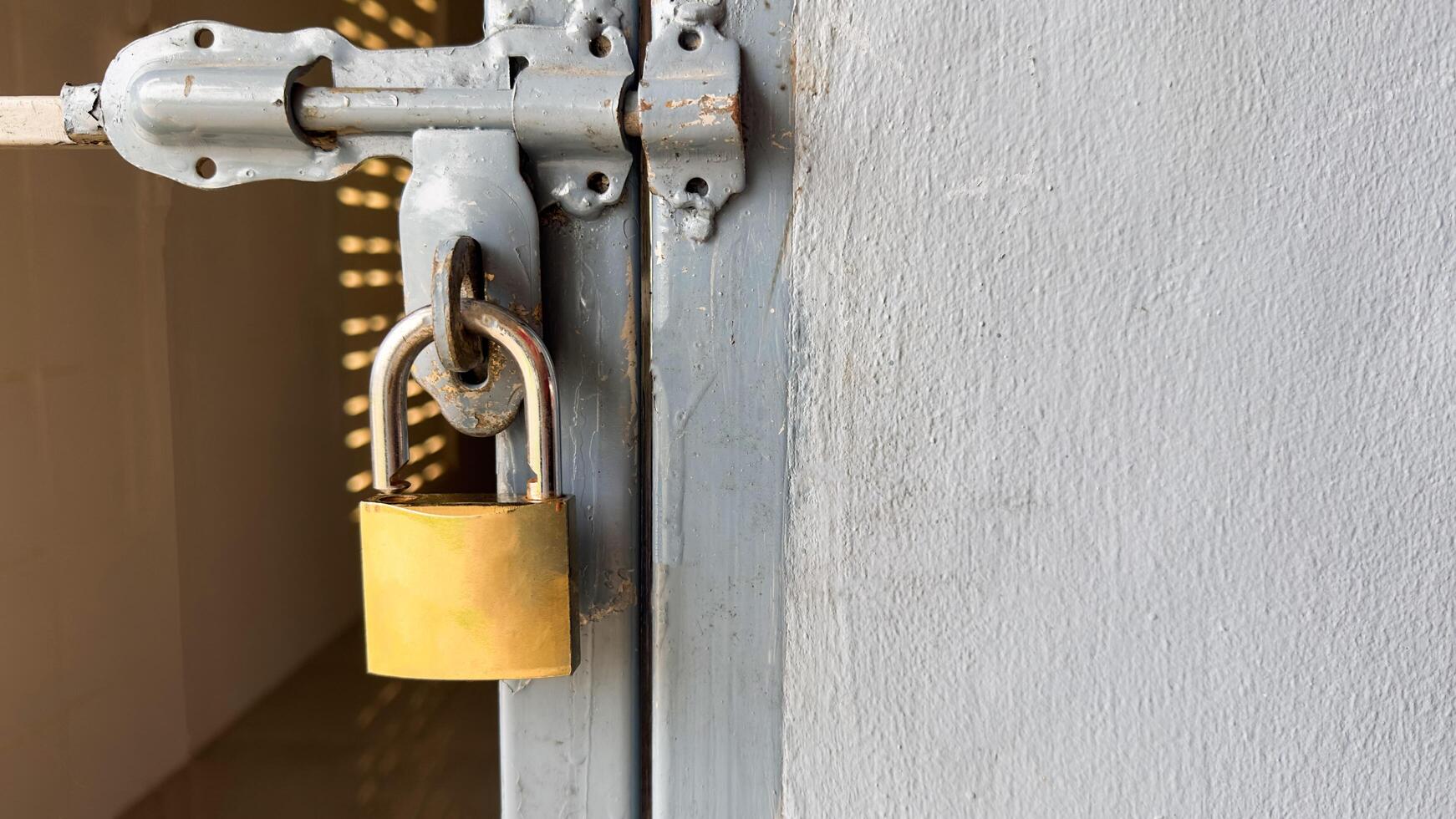 A shiny golden locking pad on a textured gray metal door, symbolizing security, protection, and reliability, creating a contrast between the key's elegance and the rugged door surface photo