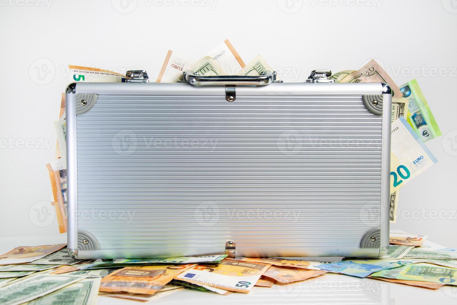 A silver suitcase is sitting on a white surface surrounded by euro and US dollar bills photo