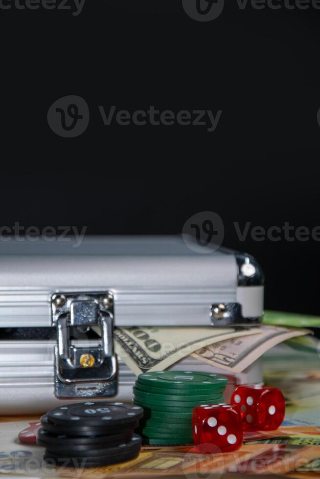 A silver case sits on top of several dollar bills with poker chips, dice, and a few more bills surrounding it photo