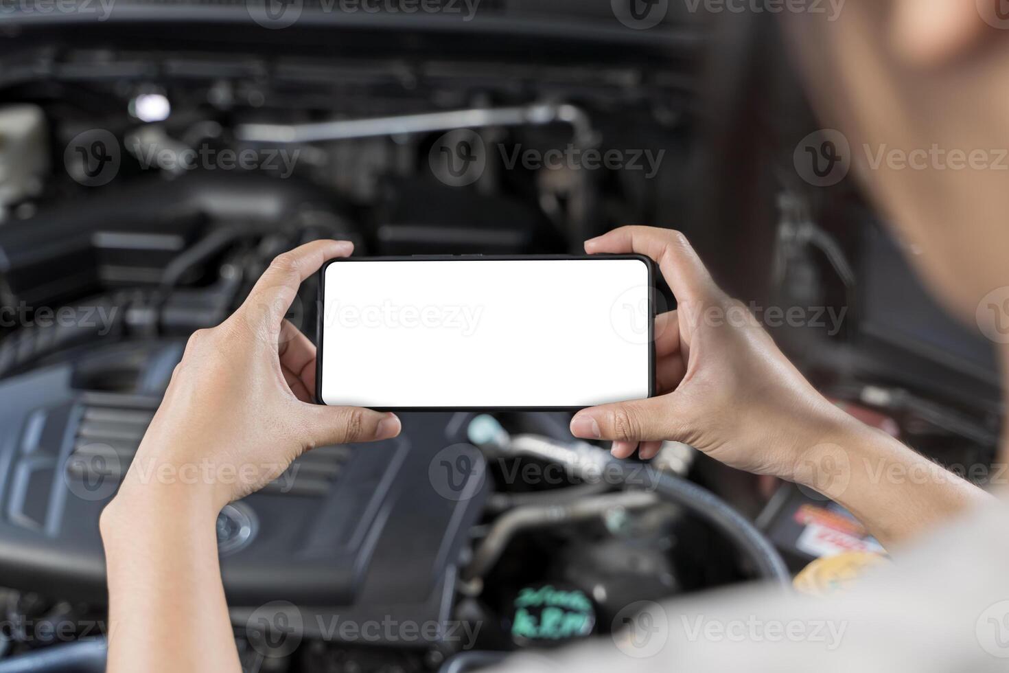Close-up of woman's hands holding smartphone with empty space on screen for your text, background of car engine. photo