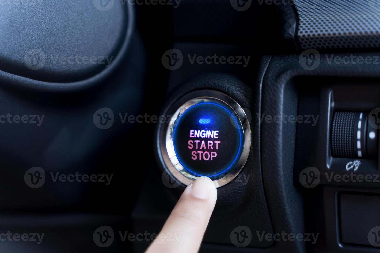 The driver palm as it presses the electric car engine start stop button with a blue light illuminated photo