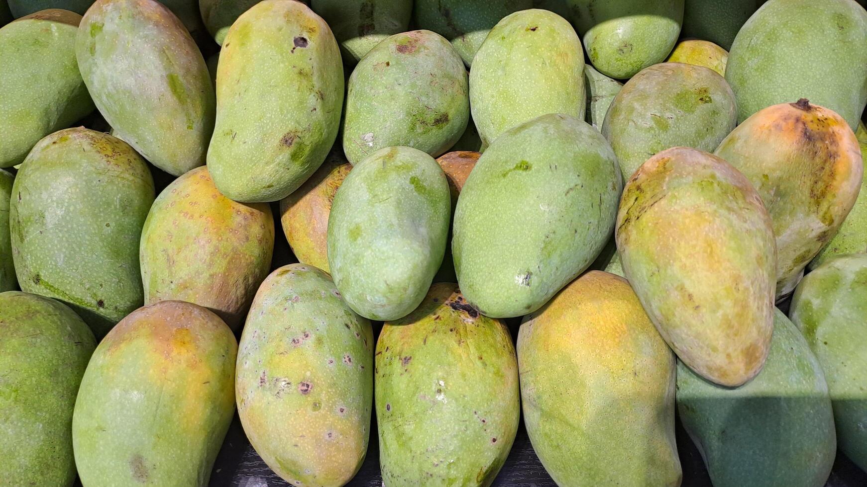 Pile of fresh mangoes with green skin, neatly arranged in a supermarket photo