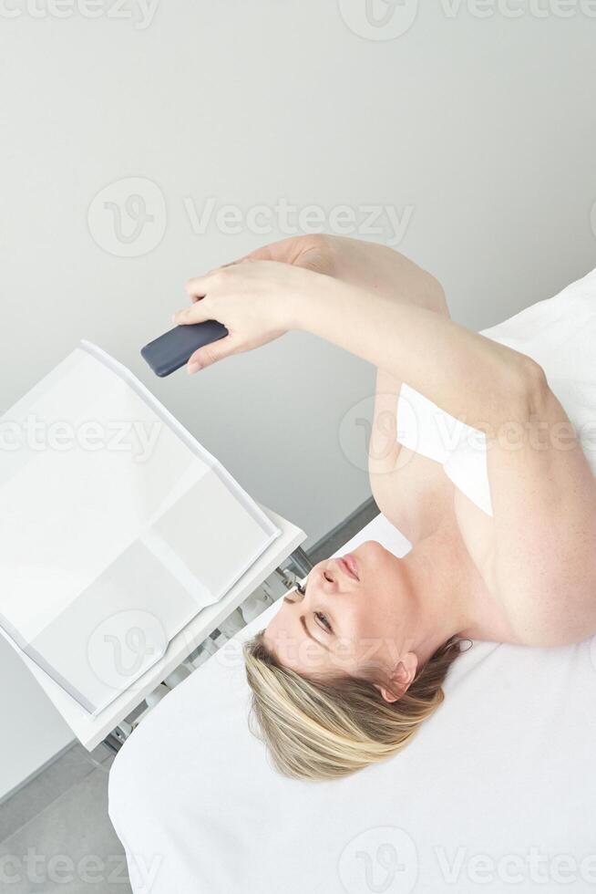 Caucasian young female using smartphone while lying on spa table in relaxing environment. photo