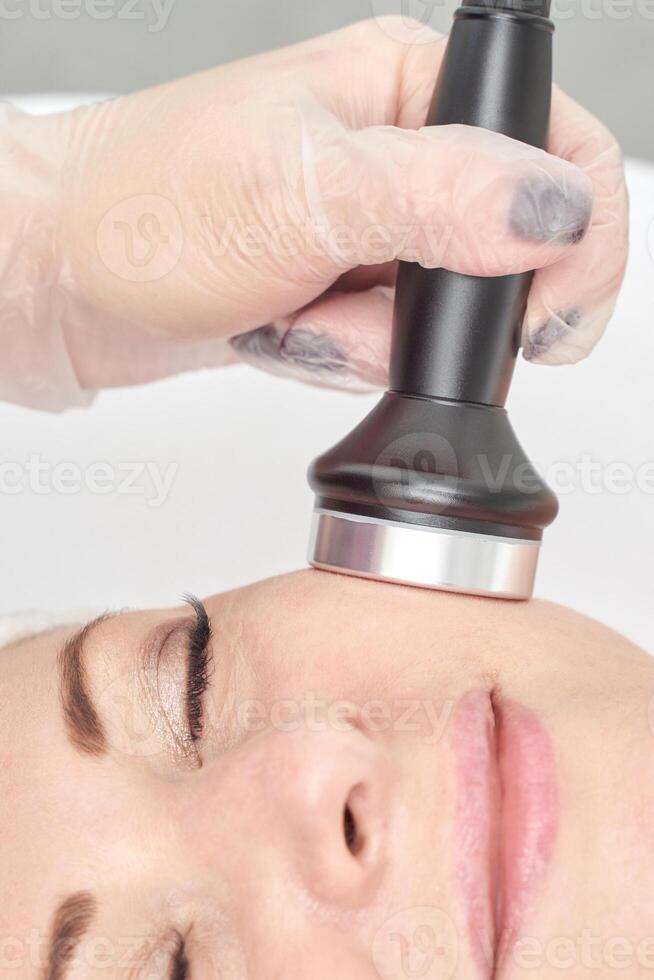 Caucasian female receiving facial treatment with ultrasound device in spa setting. photo