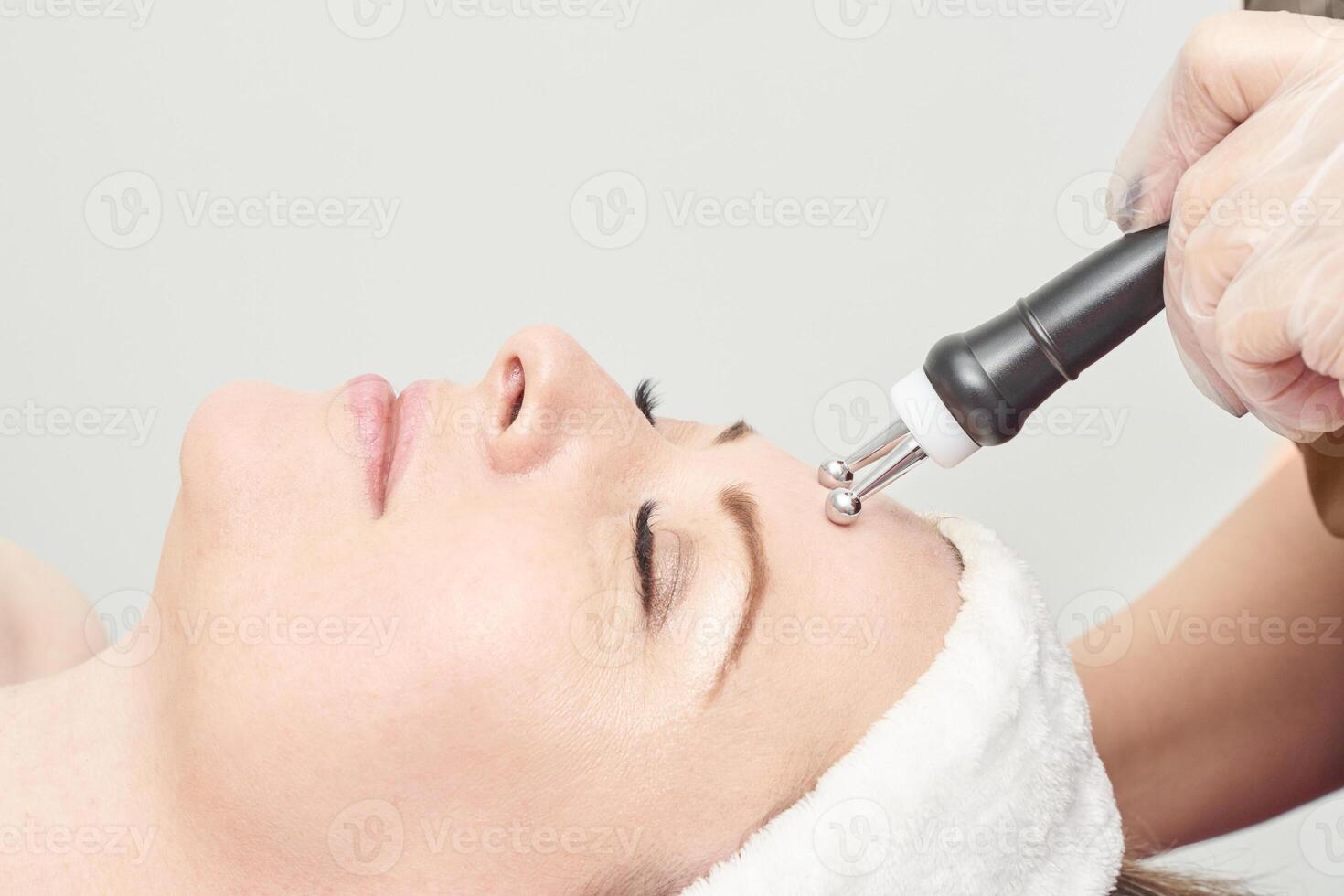 Caucasian female receiving facial microcurrent treatment in spa setting for skin rejuvenation. photo