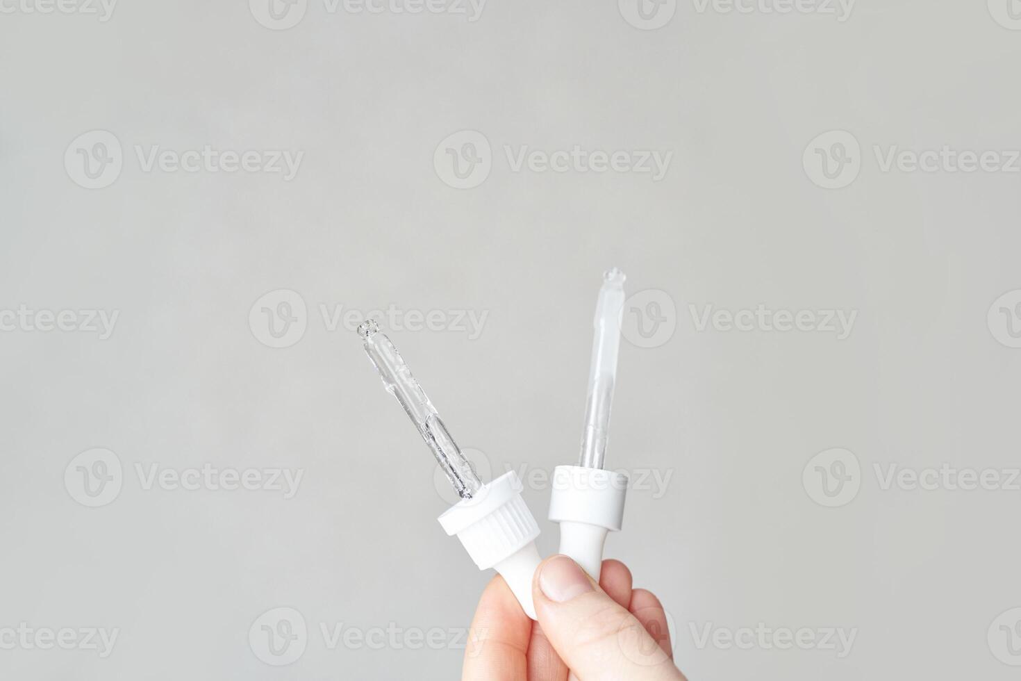 Close up of caucasian hand holding white dropper bottles against gray background. photo