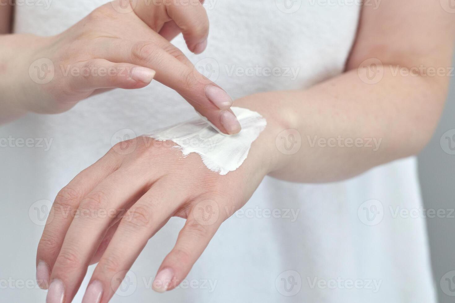 Female applying moisturizing cream on hand for skincare routine with caucasian adult hands. photo