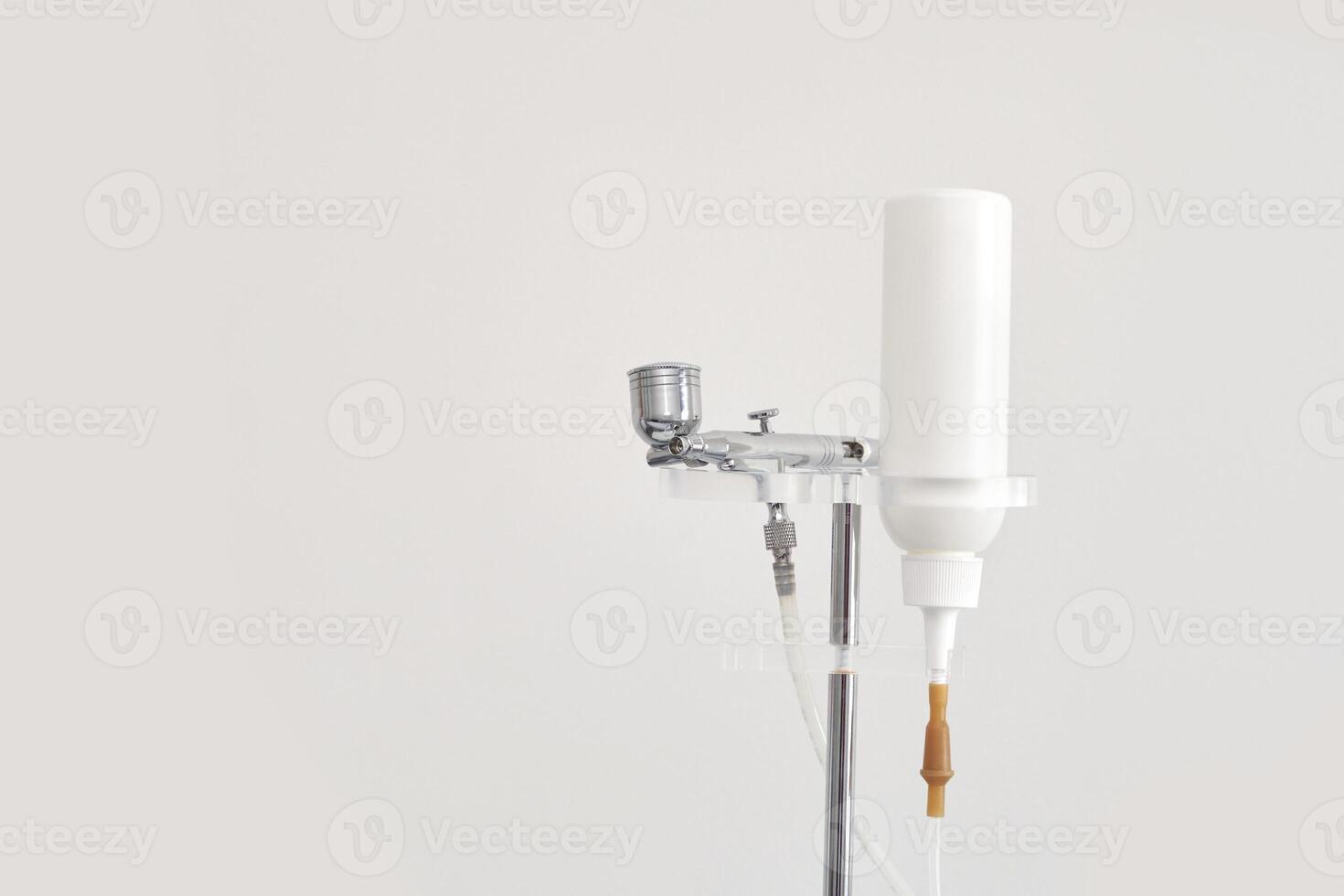 Airbrush makeup system with white bottle and metal components on stand. photo