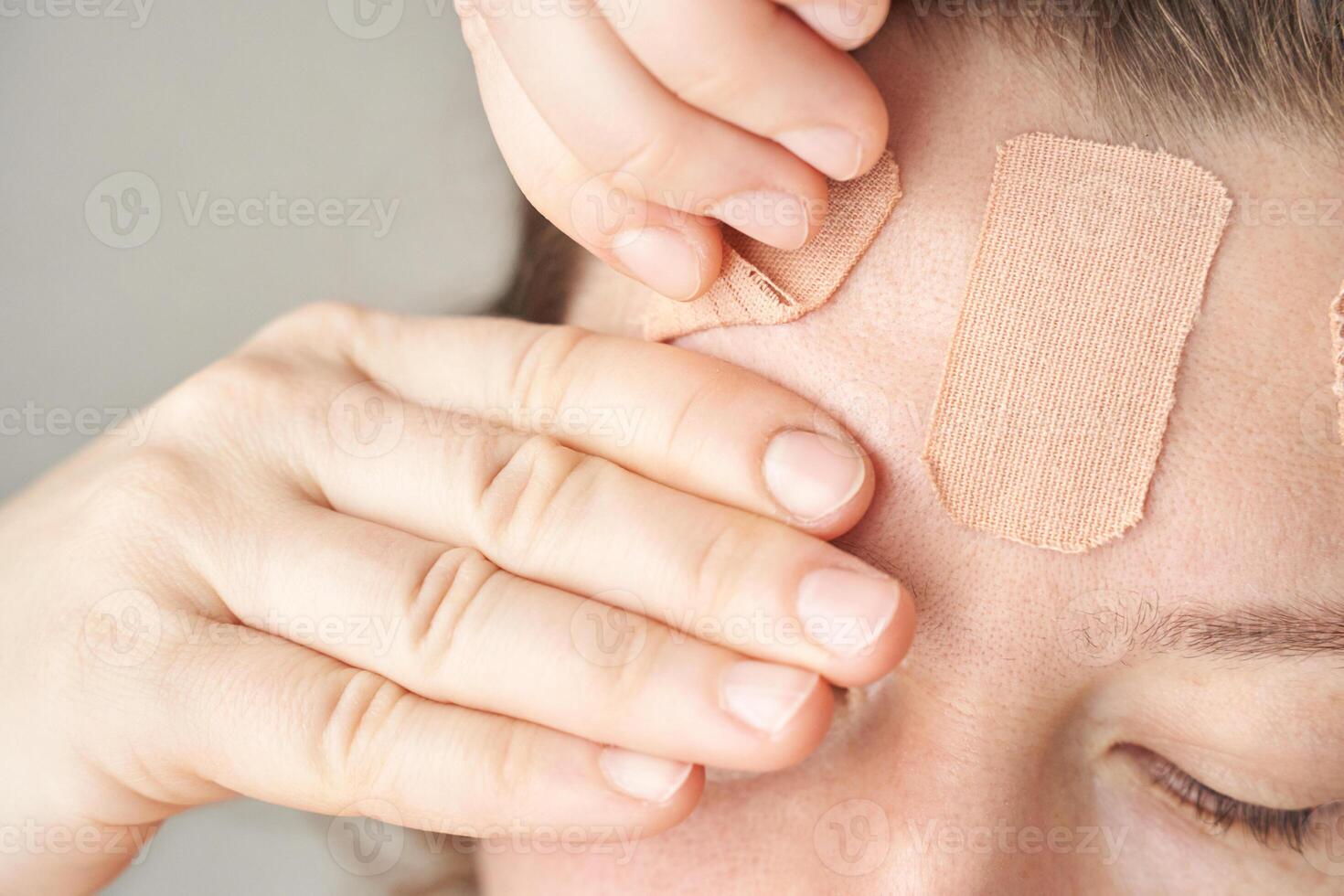 Caucasian female applying bandages to forehead with gentle hands on skin. photo