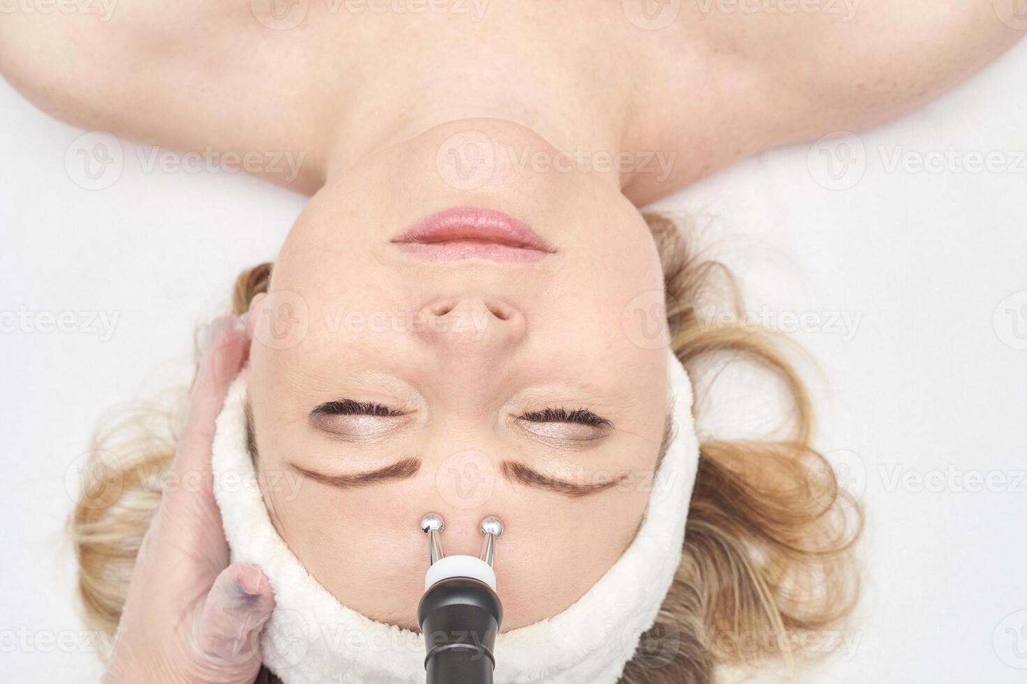 Female caucasian adult receiving facial microcurrent treatment in spa setting. photo