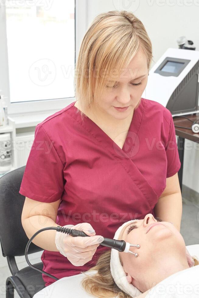 Female caucasian adult aesthetician performing facial treatment on female client with modern equipment in spa clinic. photo