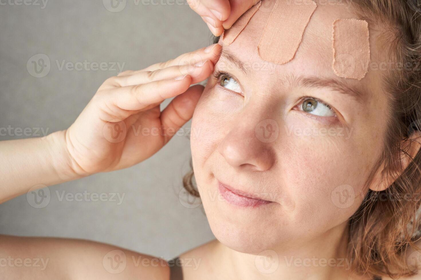 Caucasian female adult applying facial patches for skincare routine with a thoughtful expression. photo