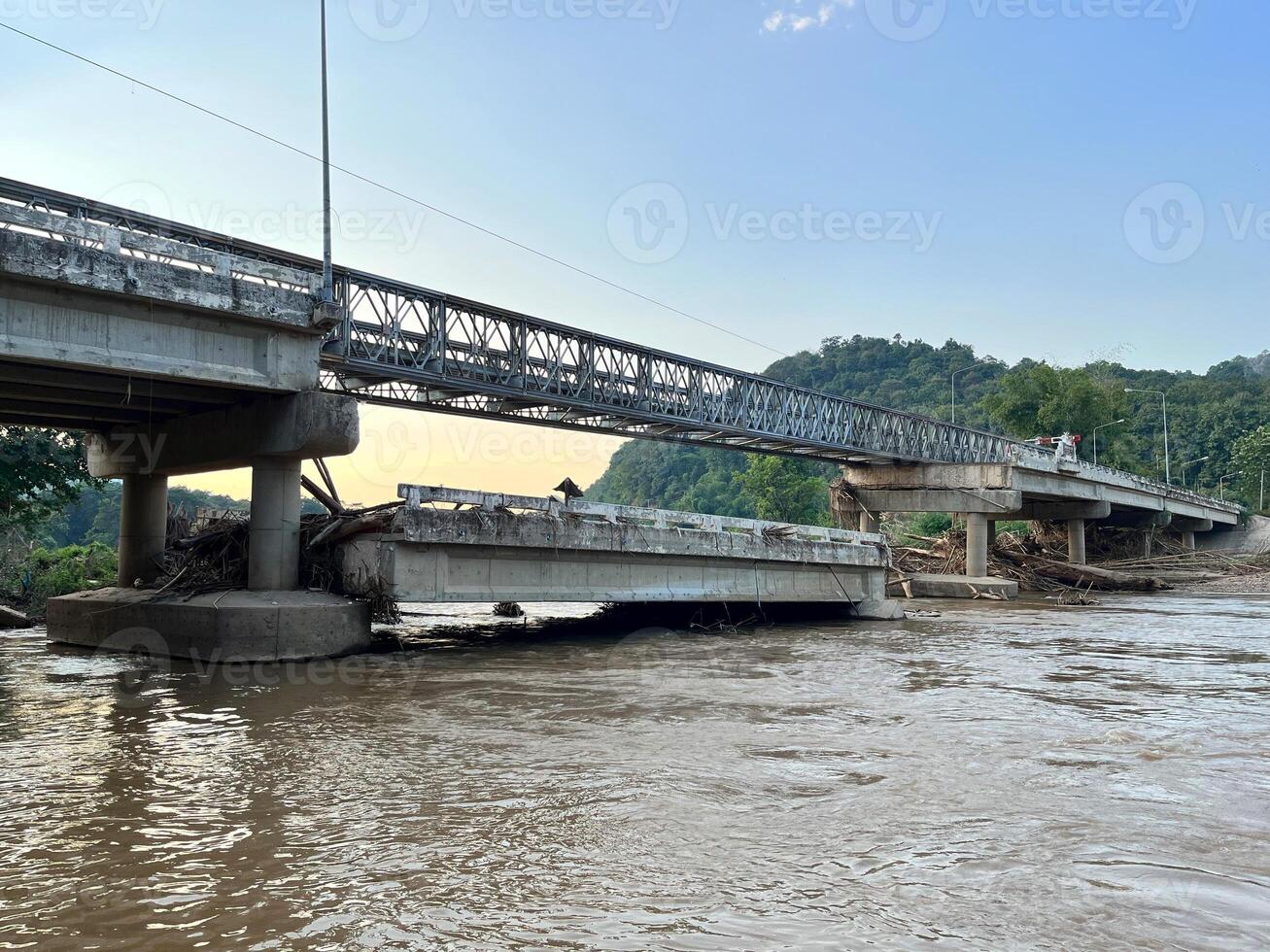 Steel bridge structure over a partially damaged or flooded river with debris accumulated below. A scene depicting infrastructure and natural forces, ideal for themes of construction, flood aftermath photo