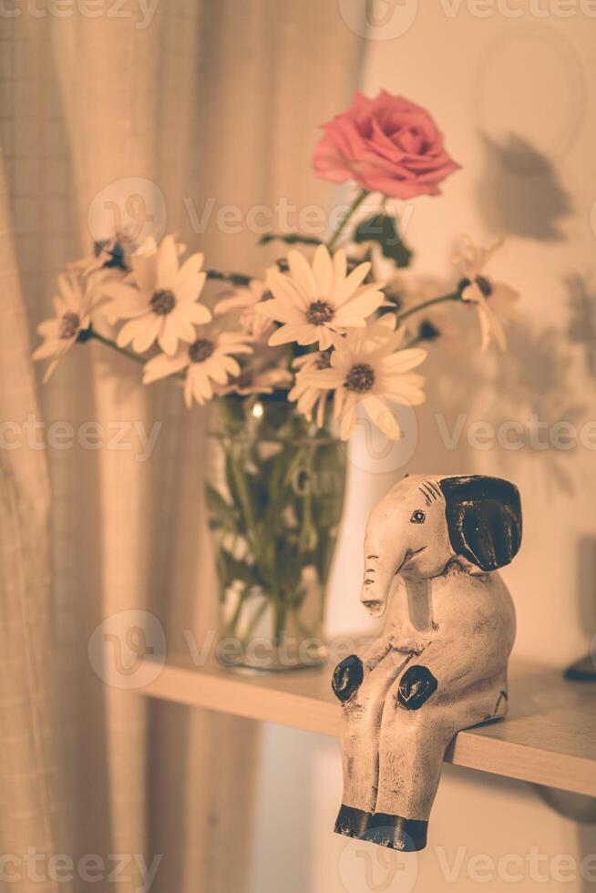 Retro still life elephant statuette sitting on shelf next to flowers in vase photo