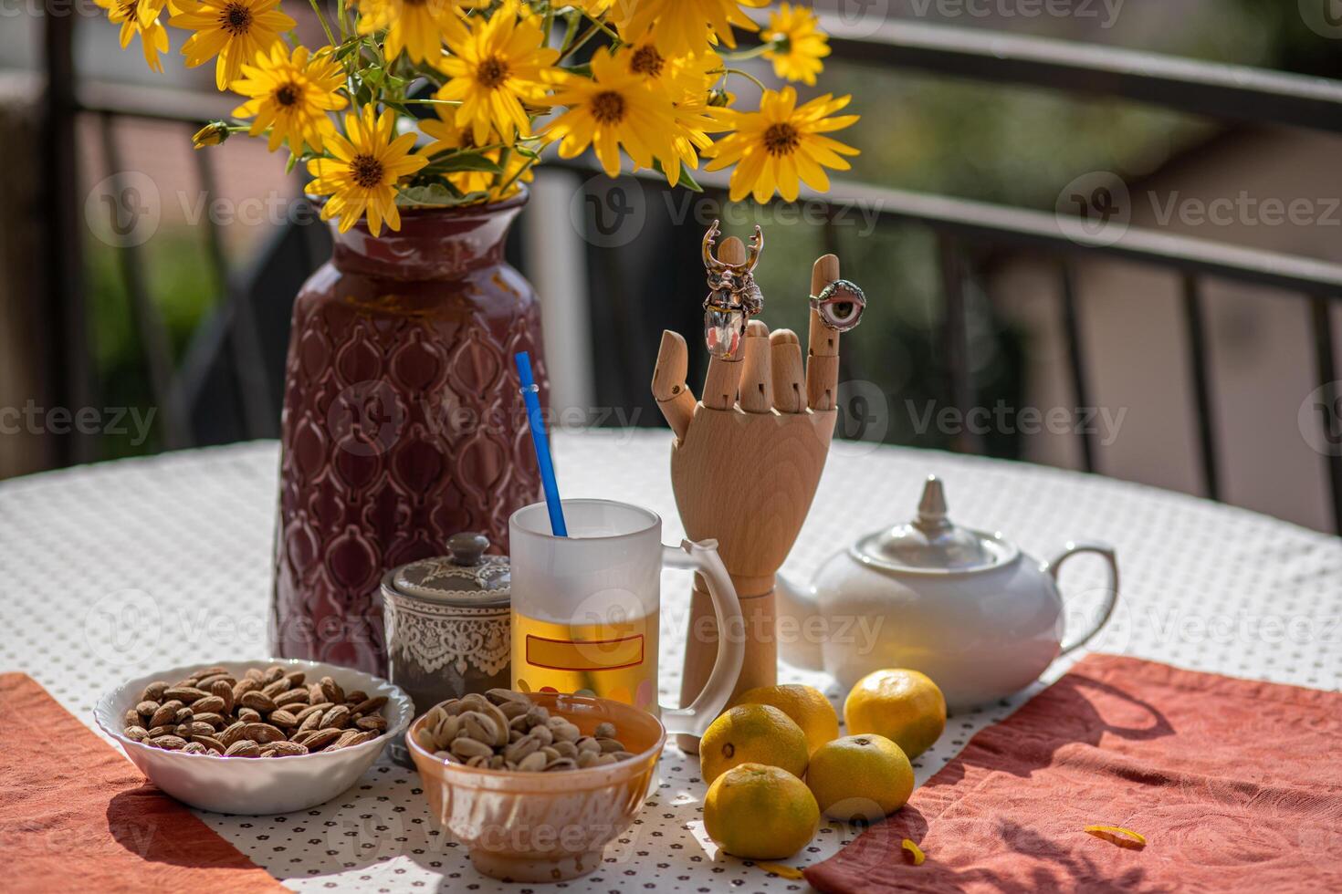 Brightly decorated table with a vase of yellow flowers, a tray of nuts, and a unique hand sculpture showcases a cozy afternoon moment outdoors in sunlight photo