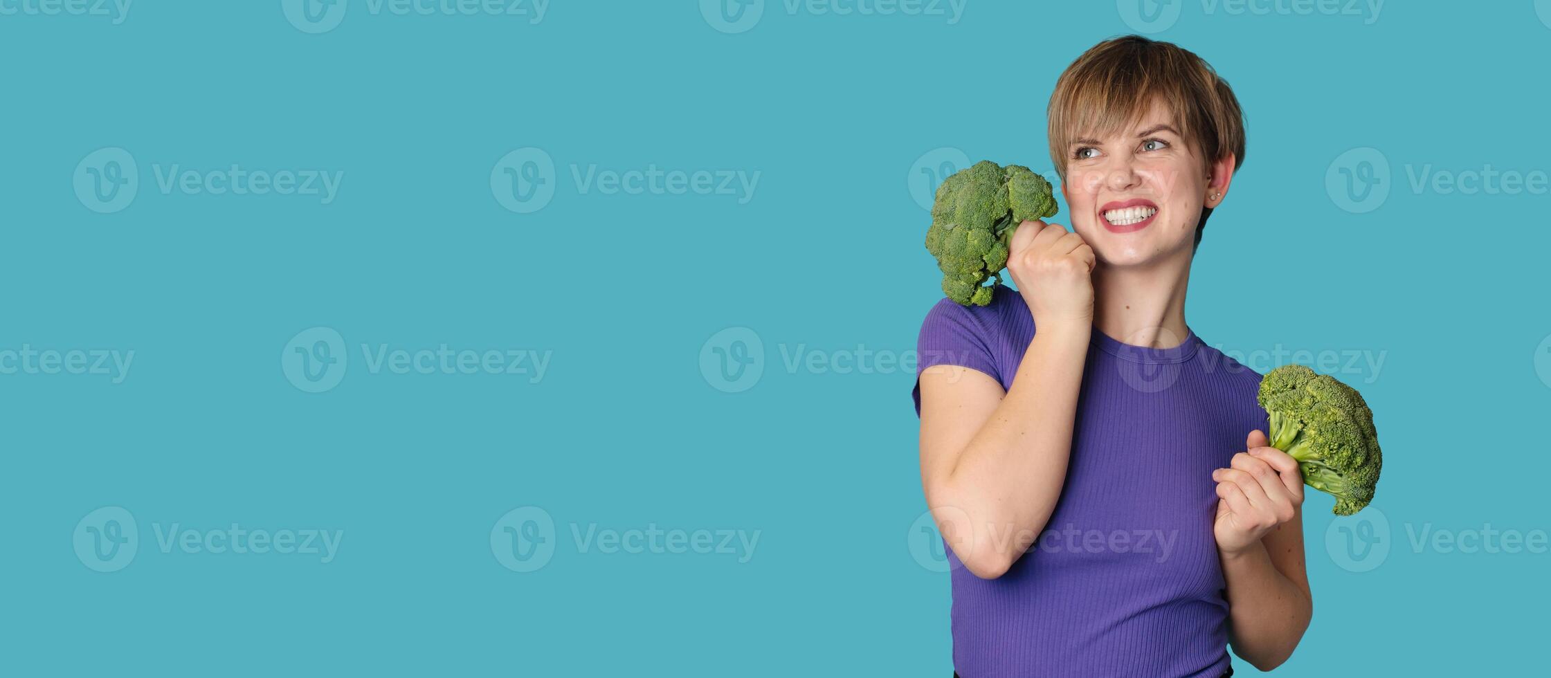 Broccoli in the hand of a slender smiling woman on a blue background. A panoramic banner with a place for your text. healthy lifestyle. photo