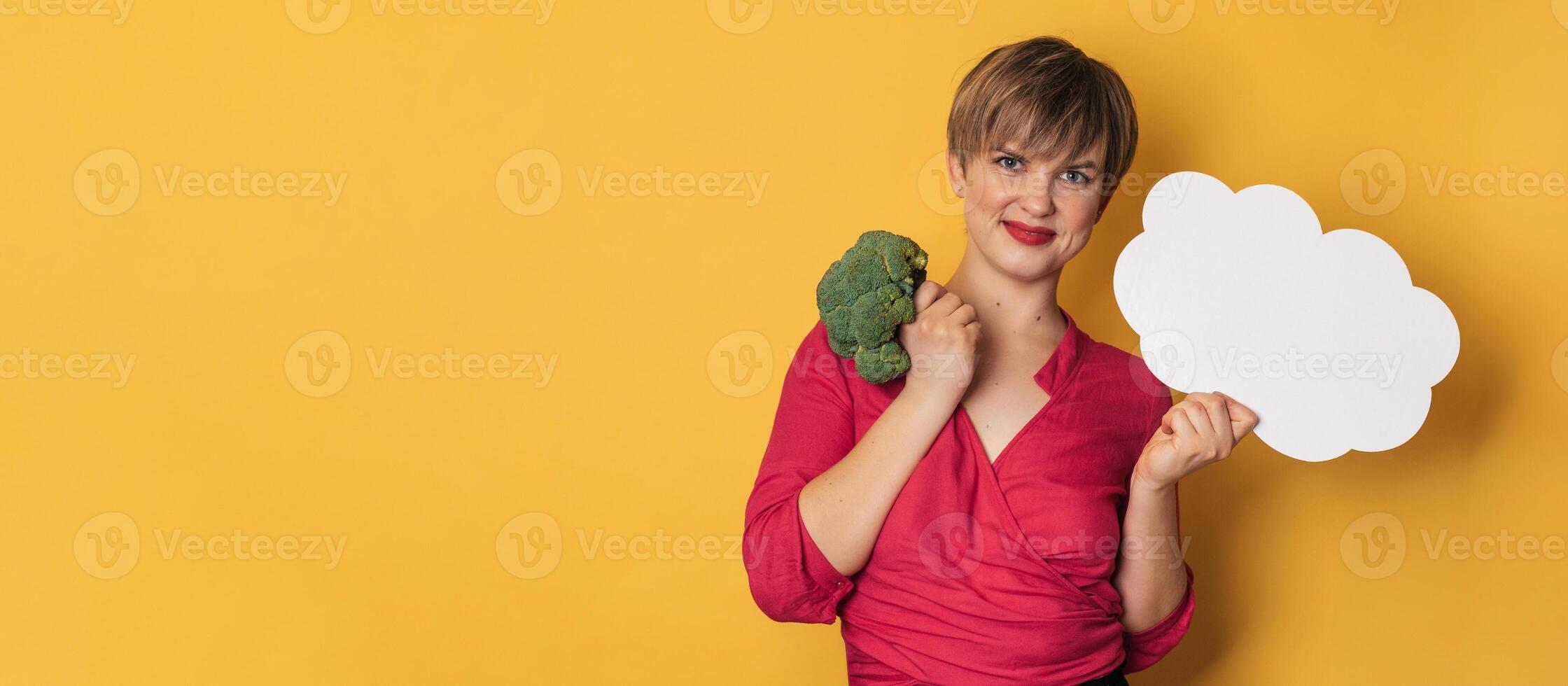 A studio shot of a young smiling woman holding fresh broccoli and a blank letterhead. The concept of healthy eating. photo