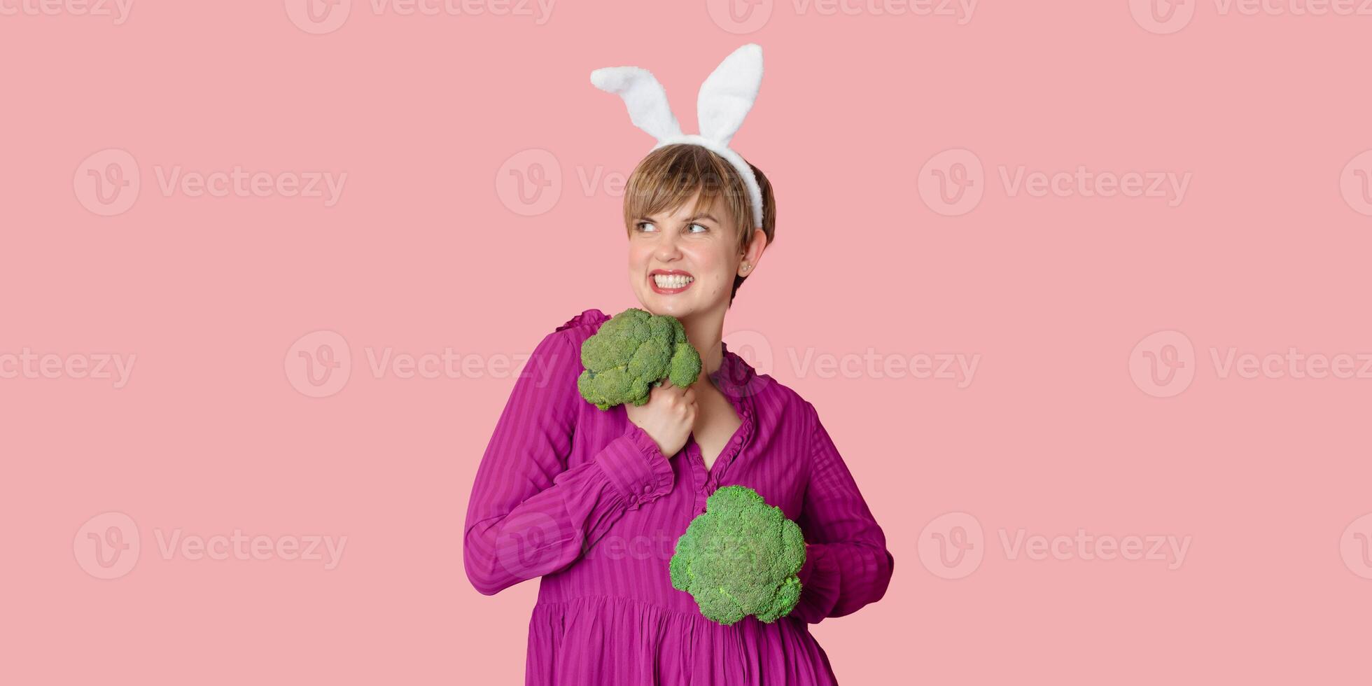 Studio shot of a young Caucasian woman in bunny ears holding organic and fresh broccoli in her hands. healthy eating.A panoramic banner with a copy of space. photo