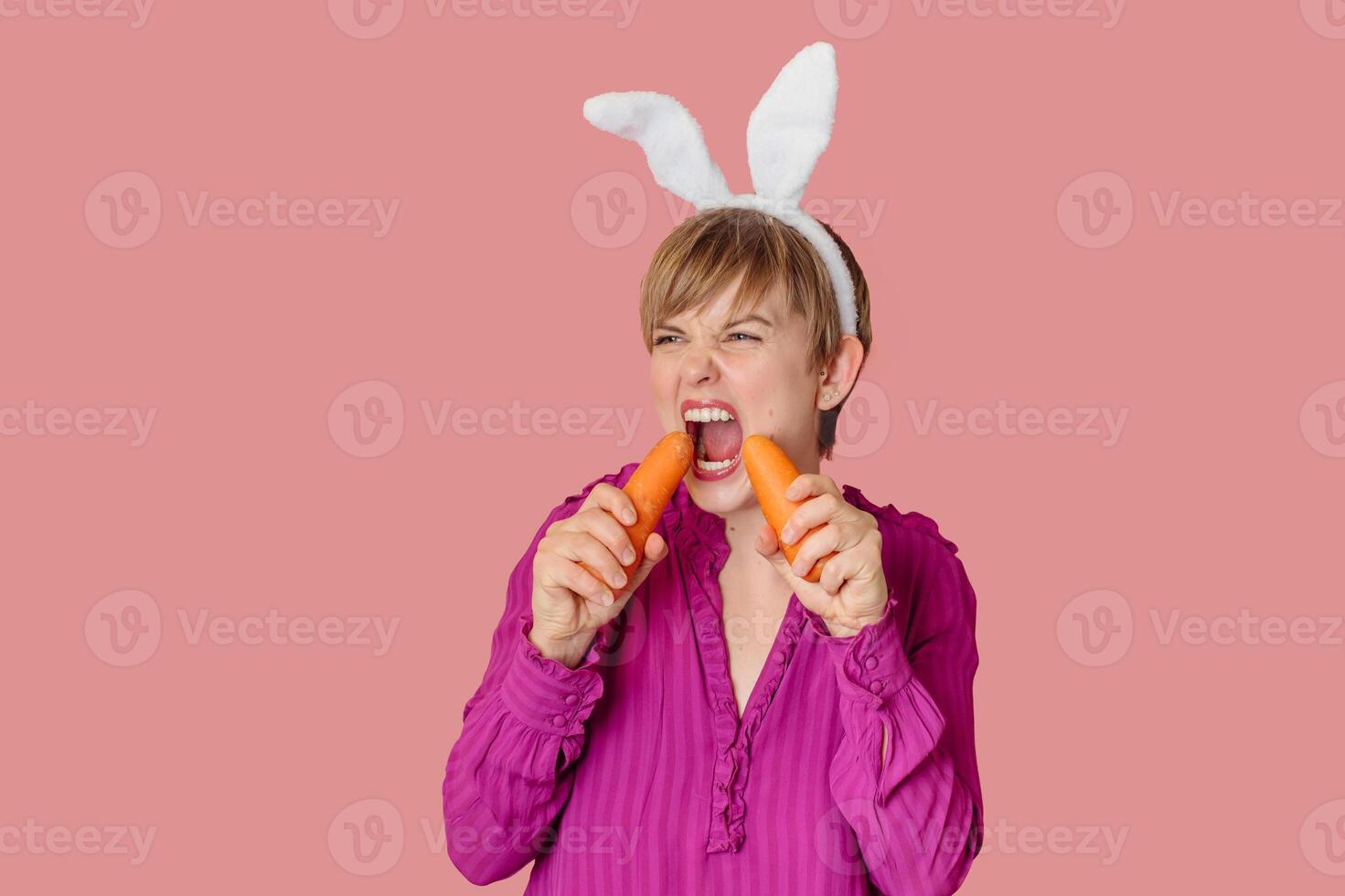 Smiling slender Caucasian girl in bunny ears with fresh carrots in her hands. Organic vegetables. photo
