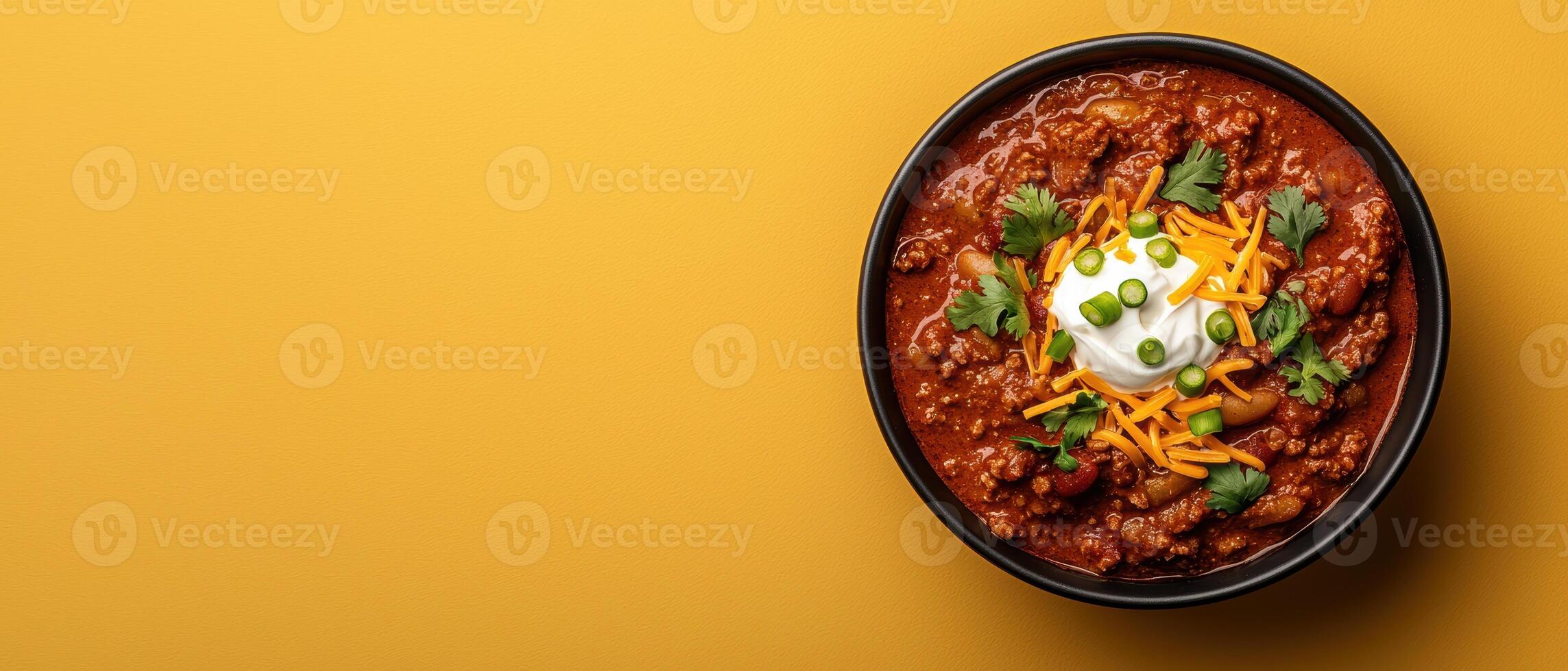 Close up of a bowl of hearty chili topped with shredded cheese, sour cream, and cilantro photo
