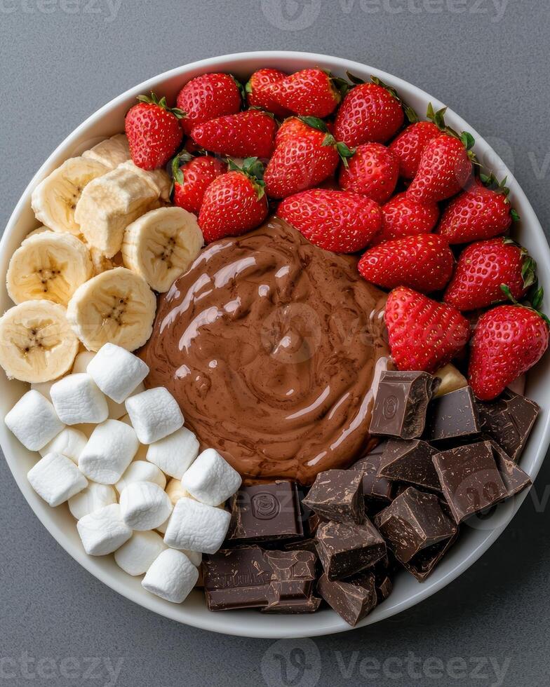 Chocolate fondue with strawberries, bananas, marshmallows, and chocolate pieces in a white bowl photo