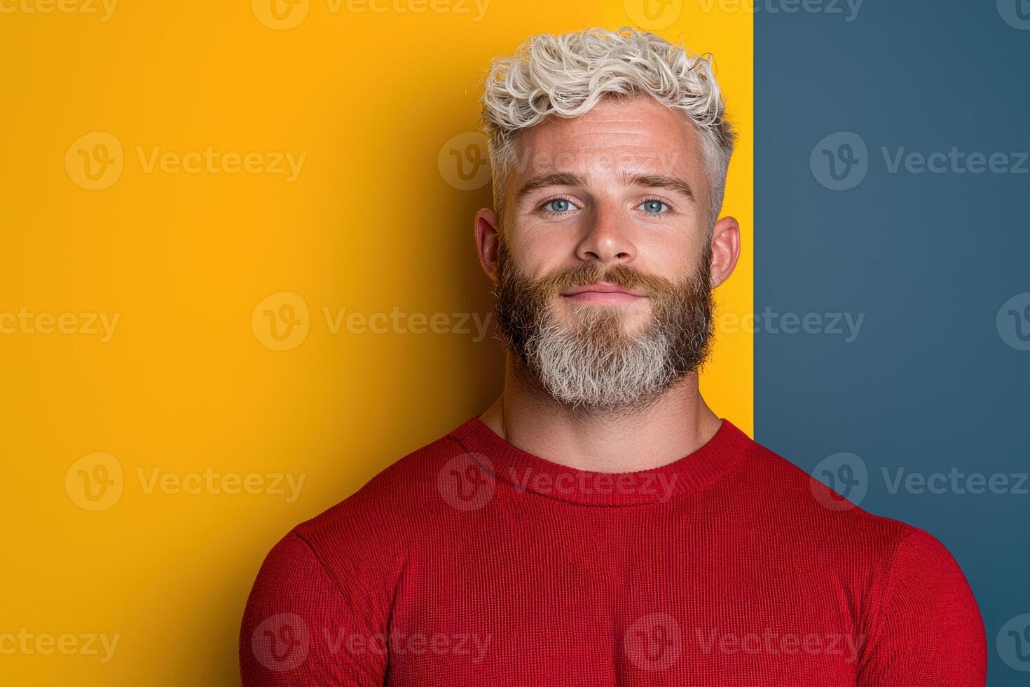 Stylish man with blonde curly hair and beard in red sweater against yellow and blue background photo