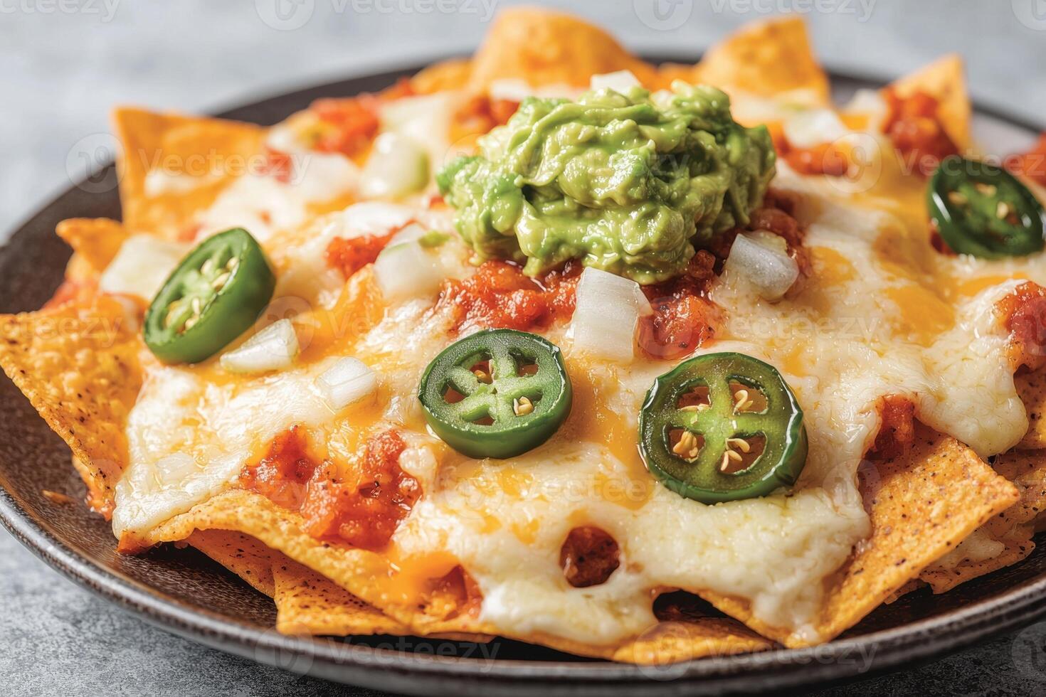 Close up of cheesy nachos with guacamole, jalapenos, and onions photo