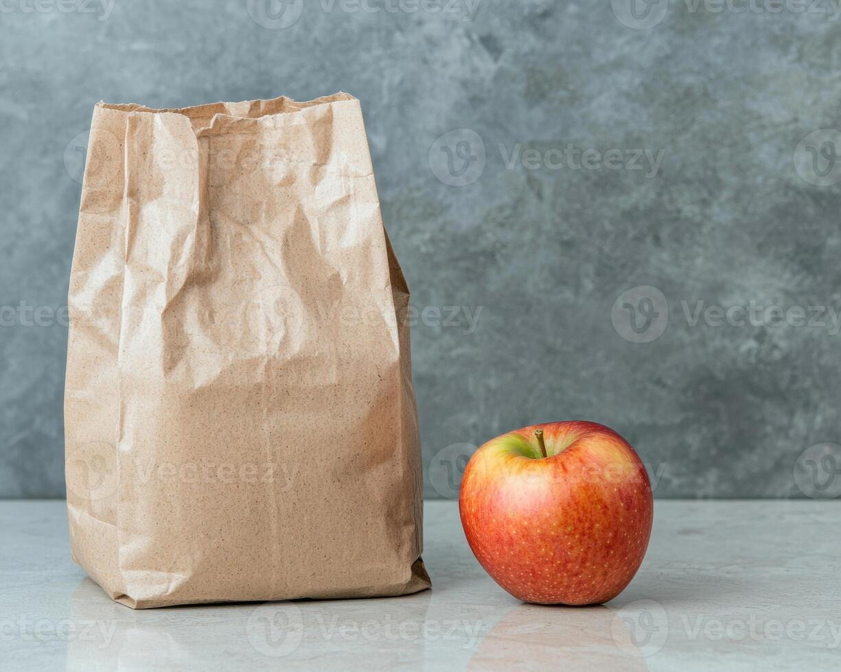 Brown paper lunch bag and red apple on a grey background photo
