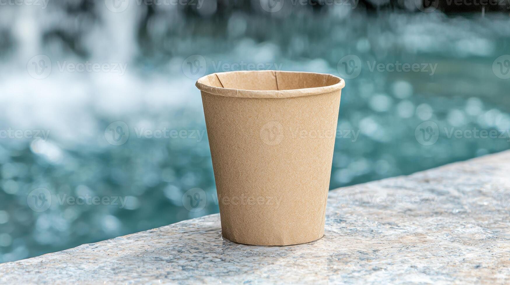 Empty compostable paper cup on a stone surface near a blurred water fountain photo