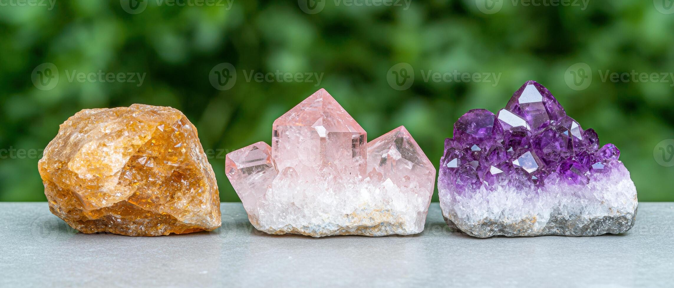 Three vibrant crystals. amethyst, rose quartz, and citrine, on a grey surface with a blurred green background photo