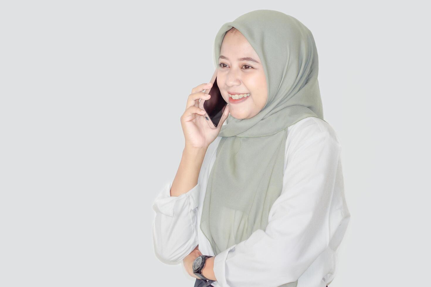 A cheerful asian woman in a light green hijab happily talks on her smartphone, exuding positivity. photo