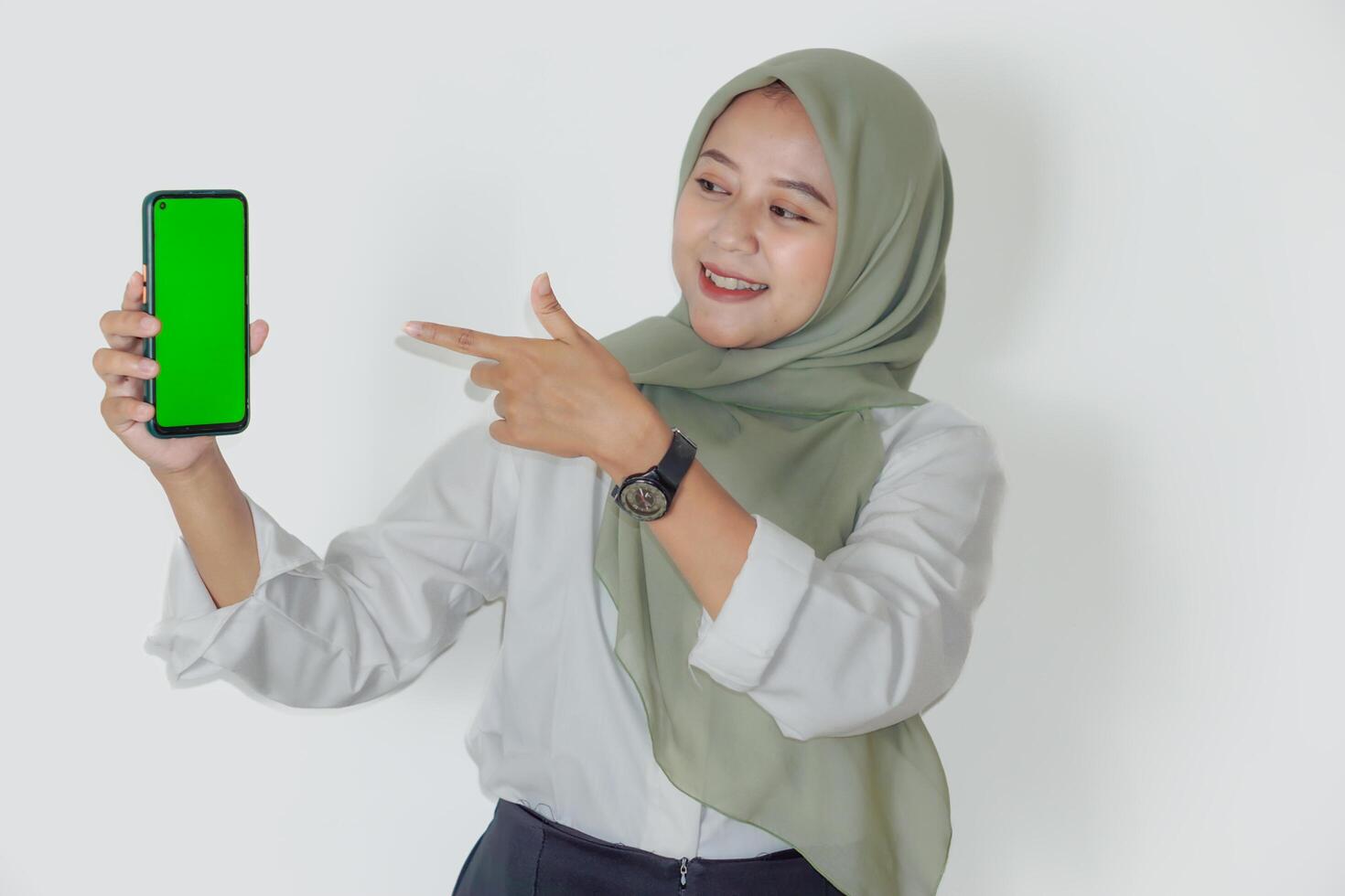 An asian woman in a green hijab smiles while showing her smartphone with a green screen. photo