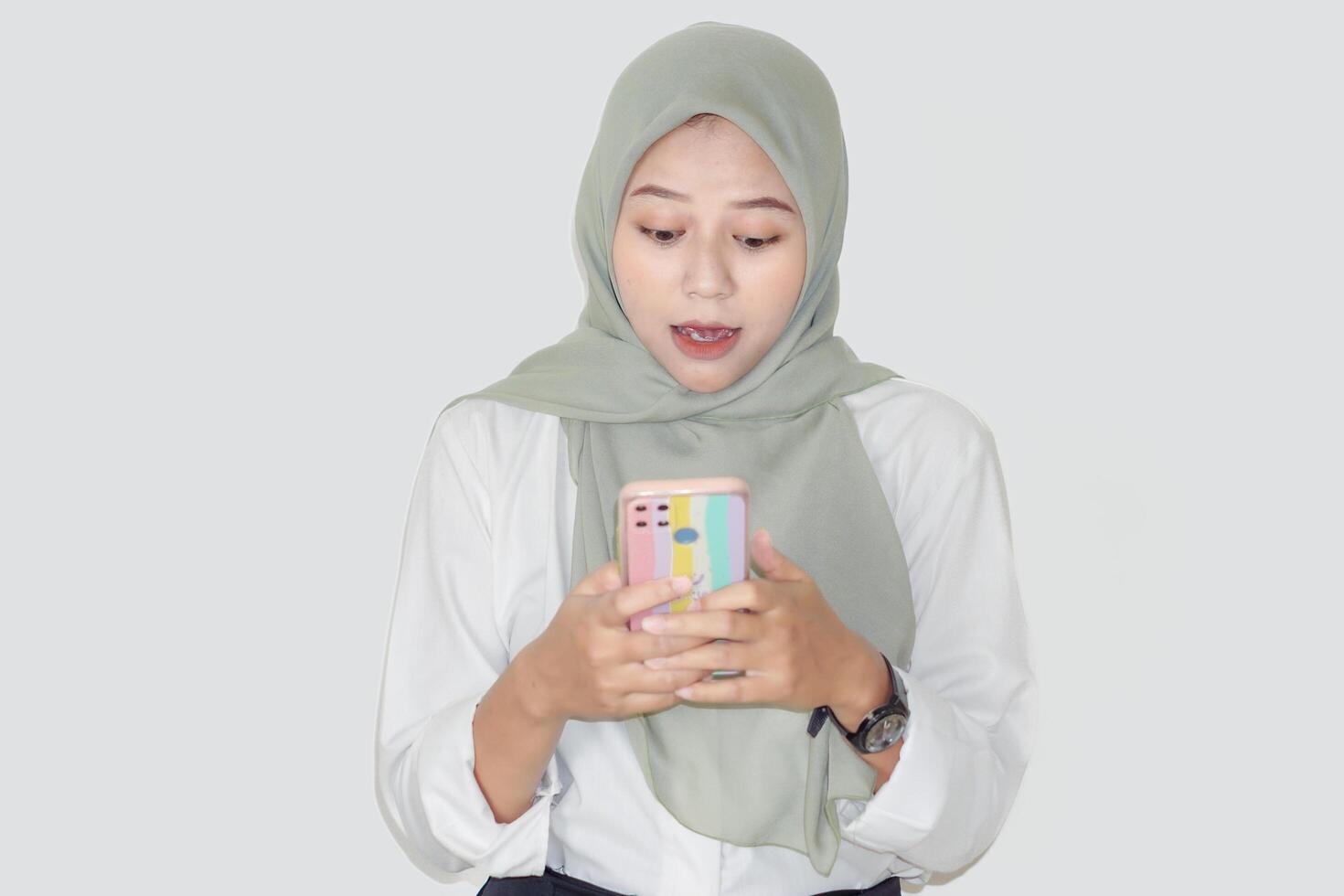 A young asian woman in a green hijab looks surprised while using her smartphone. photo