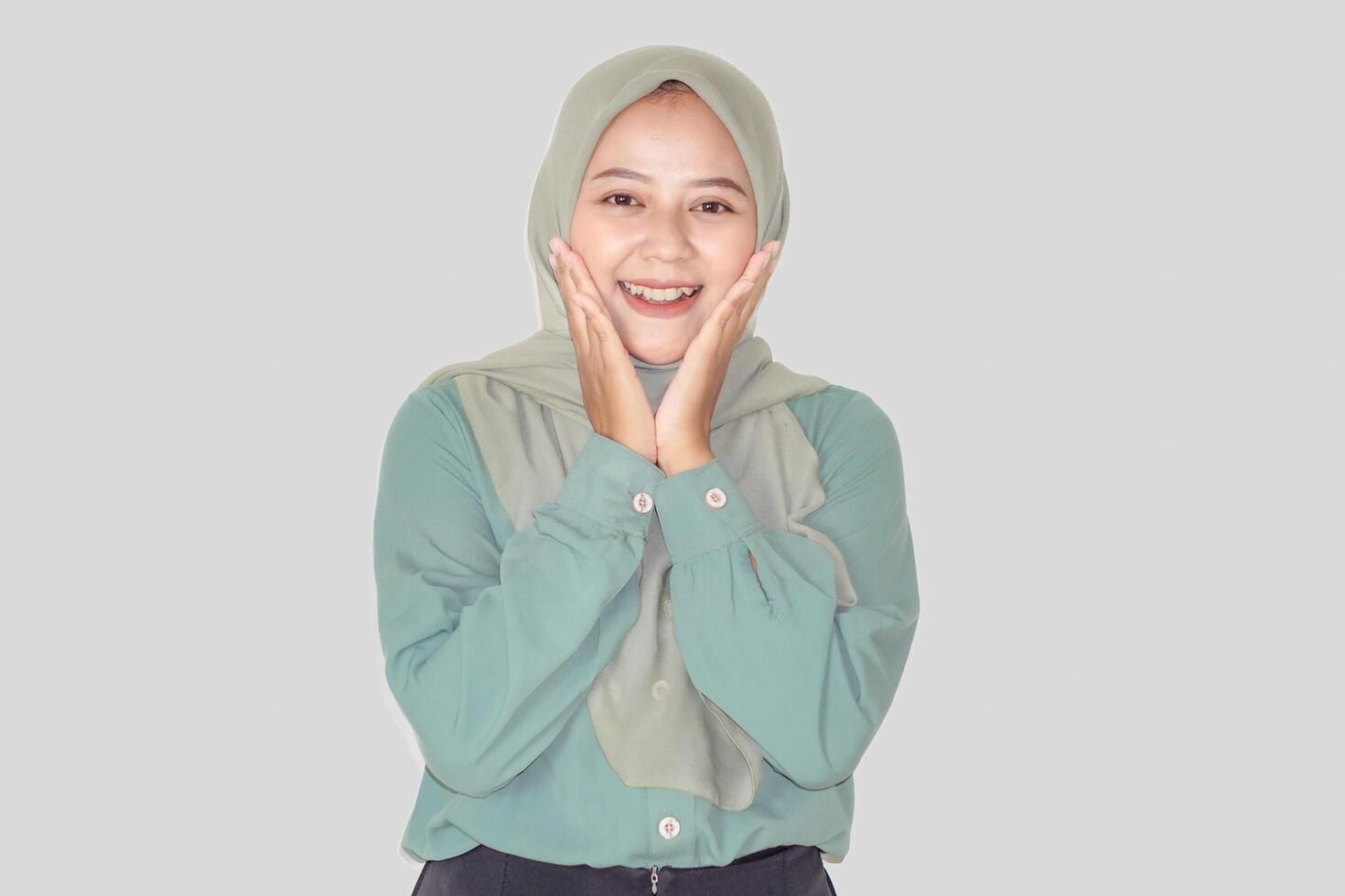 A joyful asian woman in a green outfit and hijab smiles brightly, expressing happiness and warmth. photo