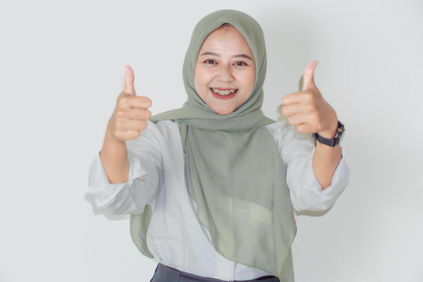 A smiling asian woman in a hijab gives a thumbs-up, exuding positivity and confidence. photo