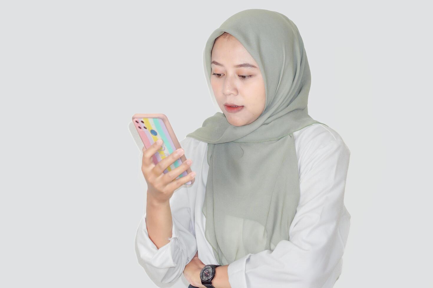 An asian woman in a green hijab intently looks at her phone, absorbed in what she is viewing. photo