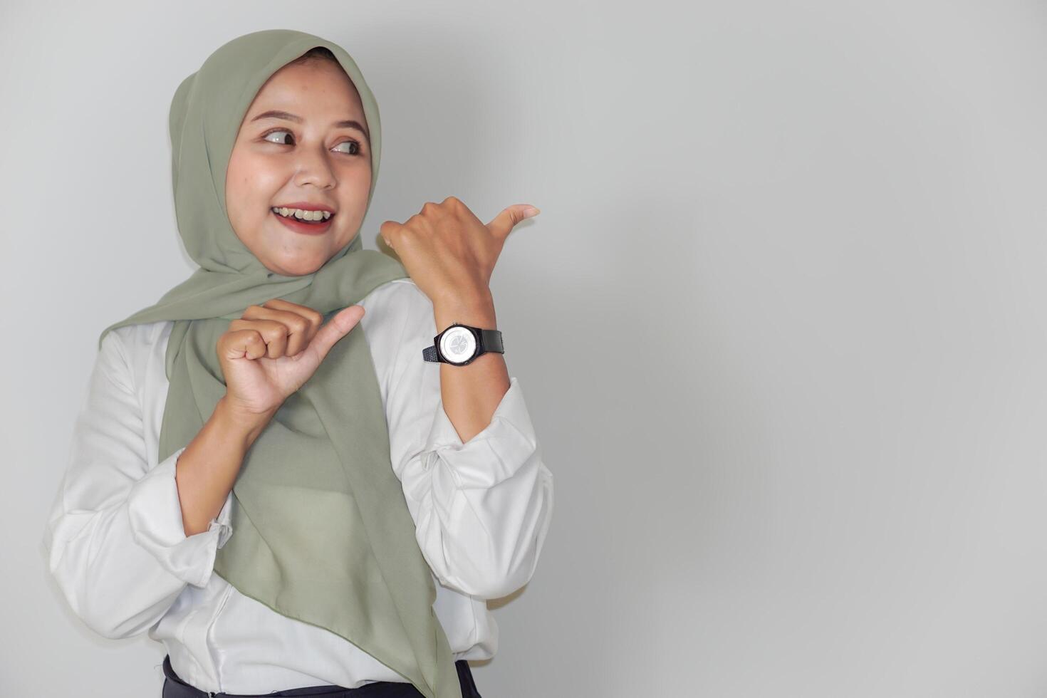 A cheerful woman in a green headscarf points to the back using her thumbs photo