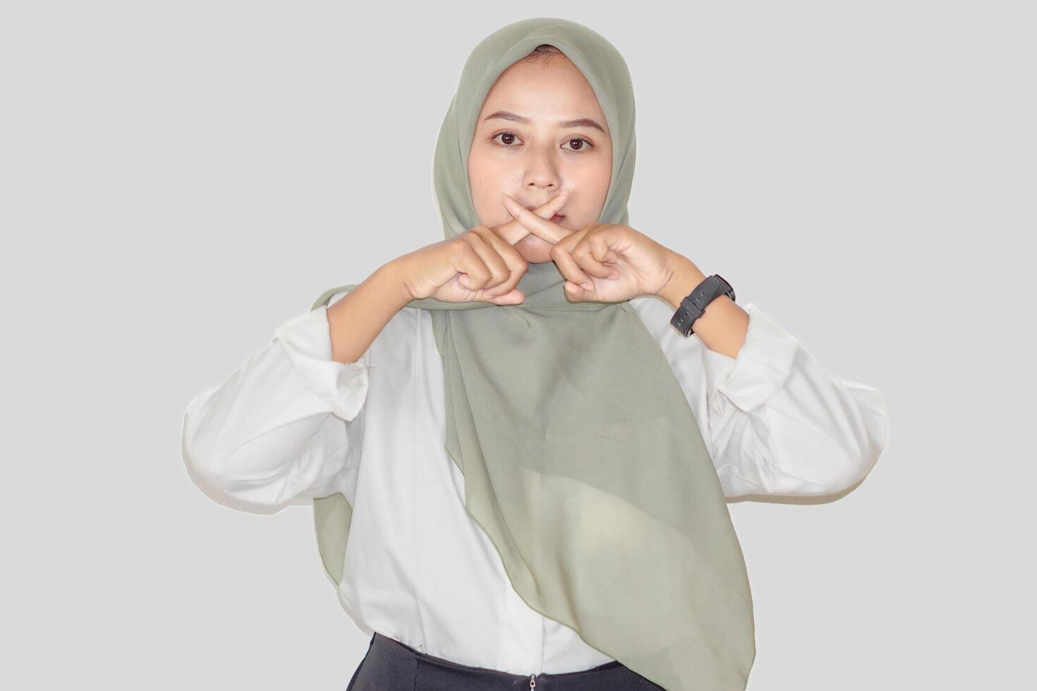 A young asian woman in a green hijab demonstrates a hand gesture, conveying a message of caution. photo