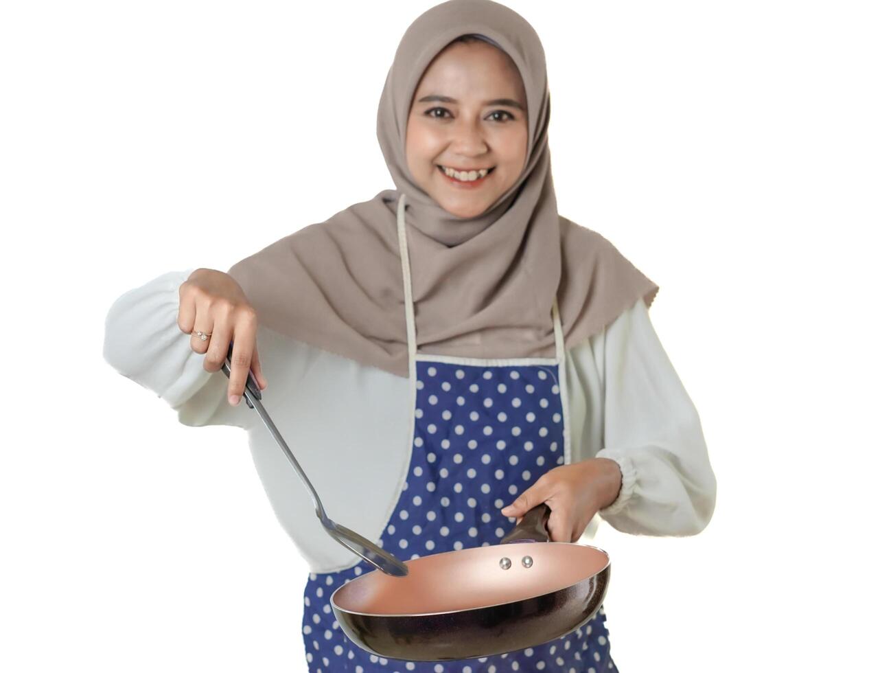 A woman in a hijab and a polka dot apron joyfully cooks with a frying pan, embodying the delight and warmth of home-cooked meals. photo