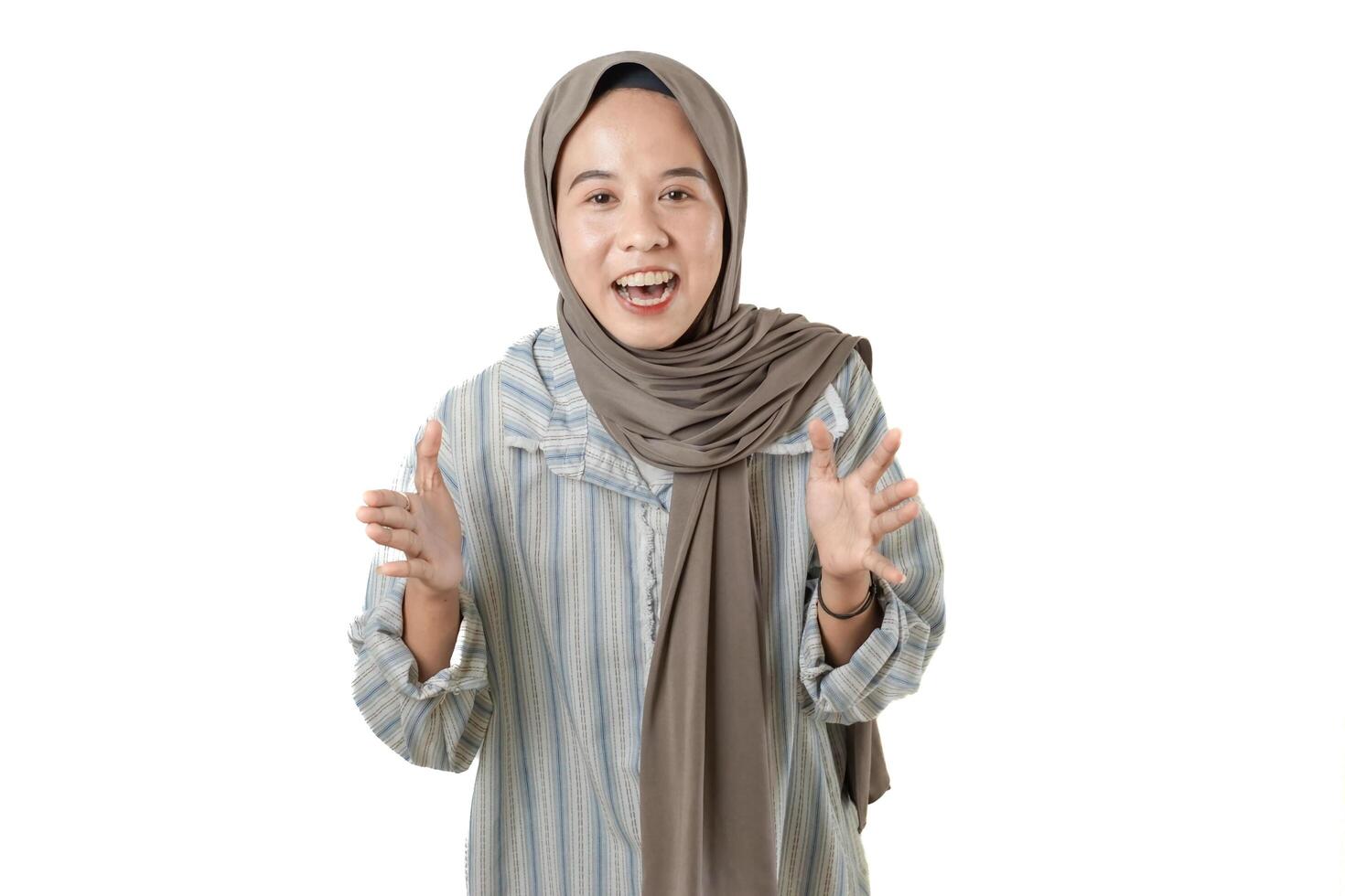A cheerful woman with a light gray hijab and a striped shirt gesturing enthusiastically, conveying a message or telling a story on a white background. photo
