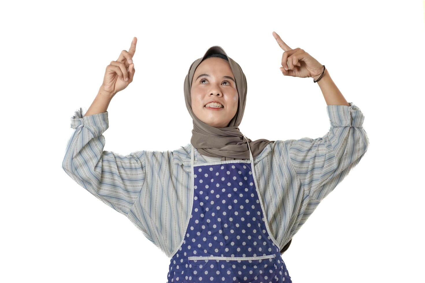 A smiling woman wearing a headscarf and polka dot apron points upwards photo