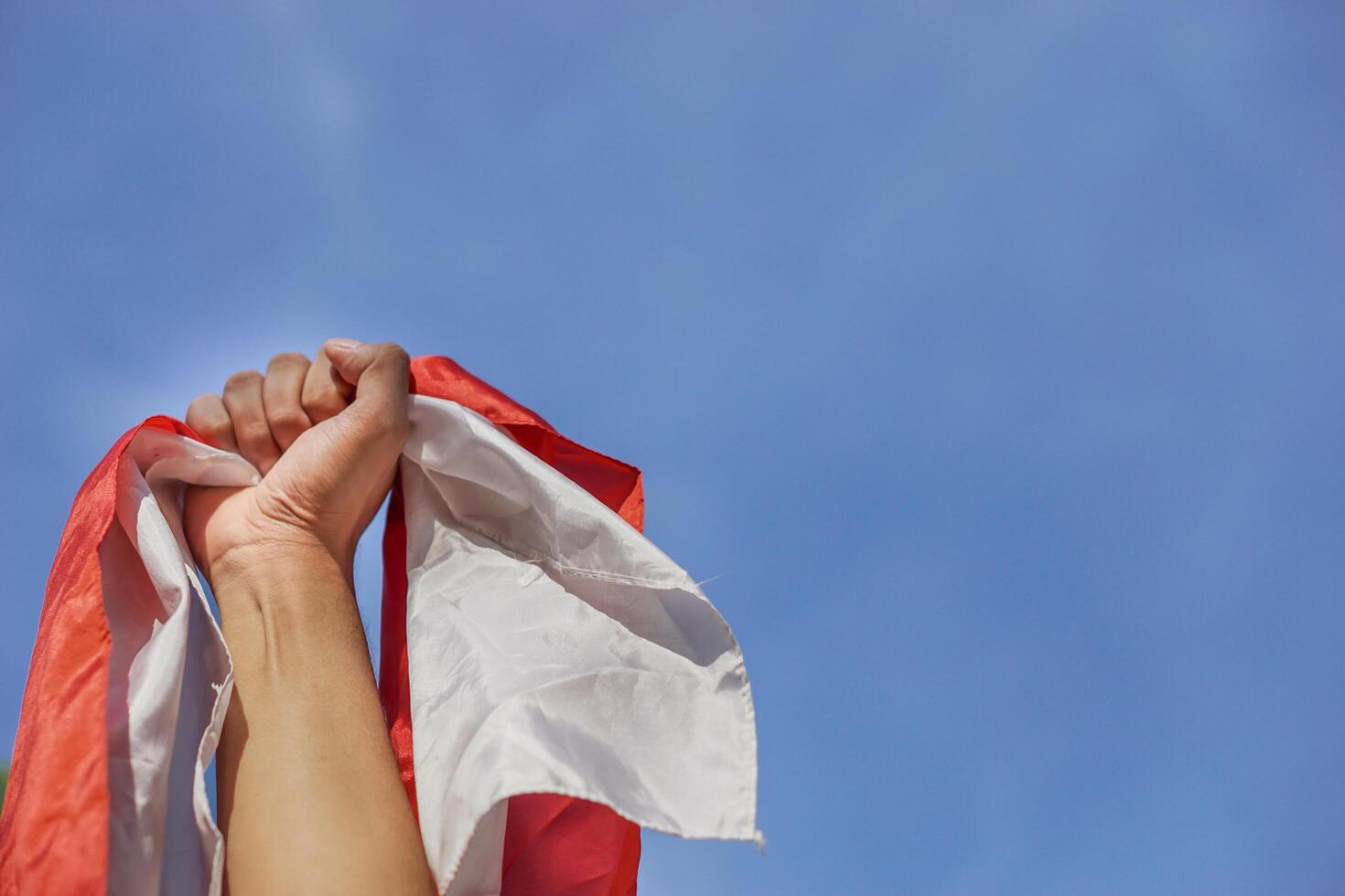 A hand proudly waves the Indonesian flag against a clear blue sky, symbolizing national pride and unity. photo