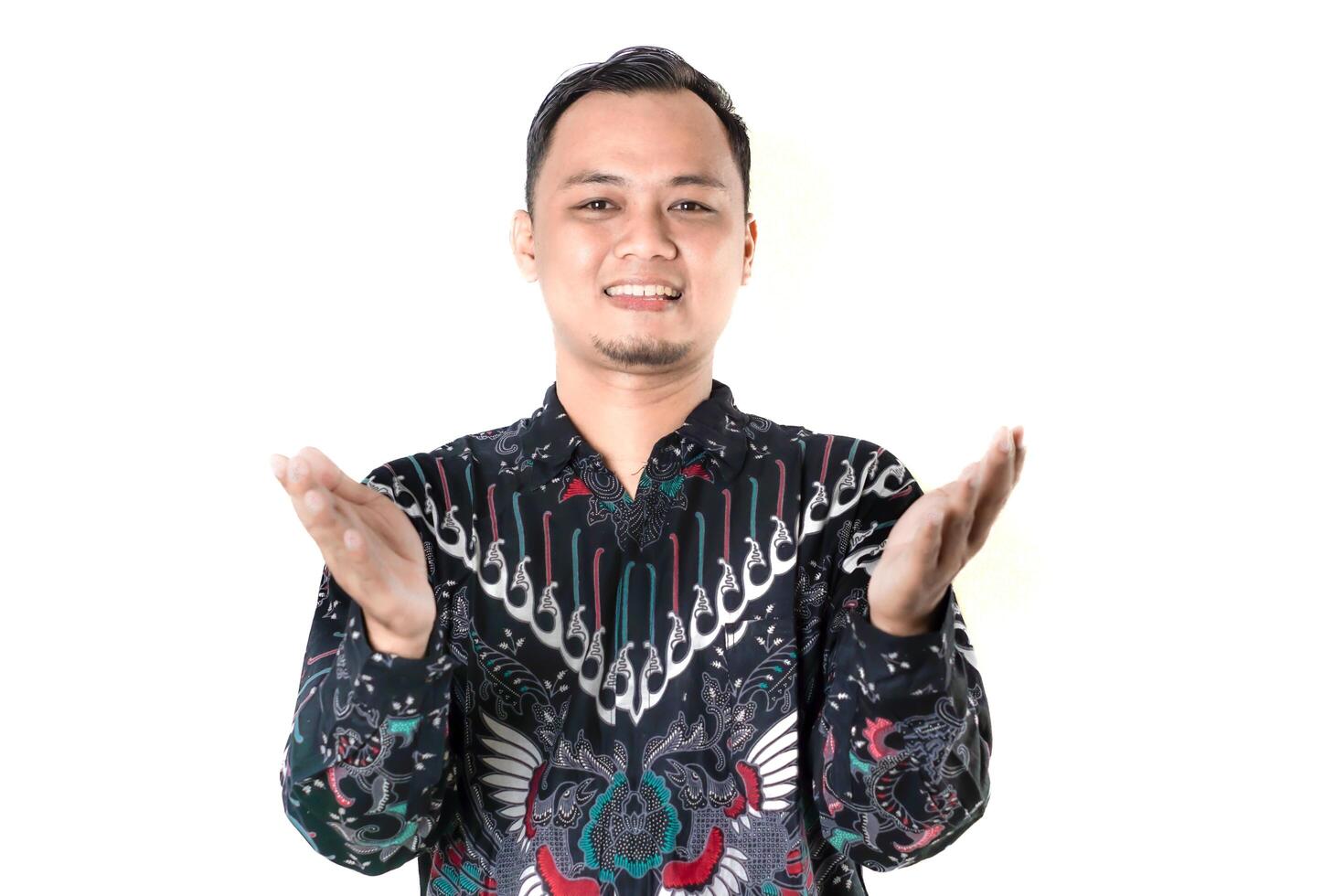 Smiling Man in Traditional Batik Shirt with Open Hands Gesture on White Background photo