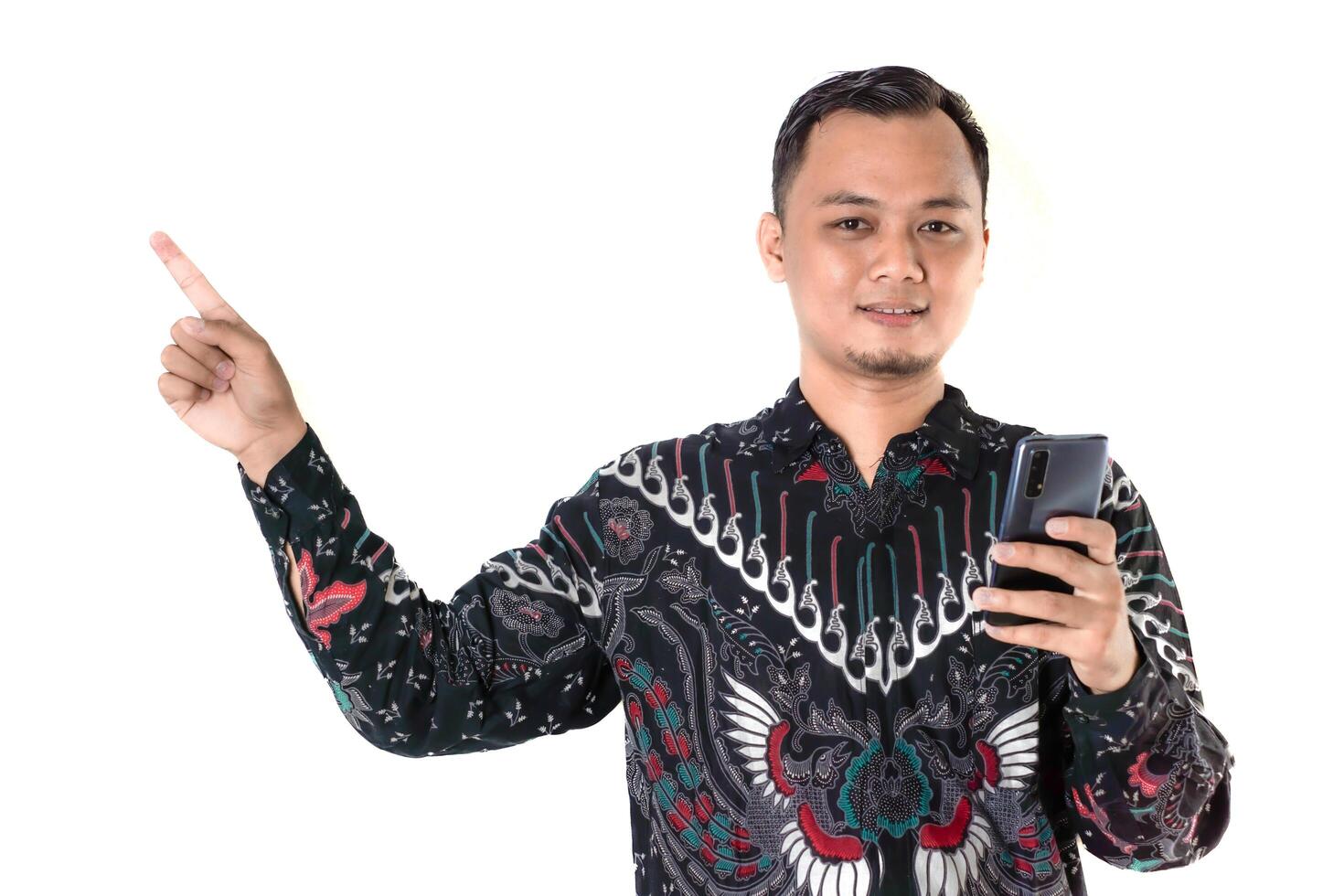 Man in Batik Shirt Pointing While Holding a Smartphone with a Cheerful Smile photo