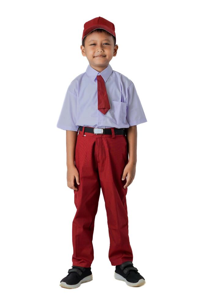 A Indonesian young boy in a school uniform smiles confidently. He wears a red cap, red tie, and red pants. photo